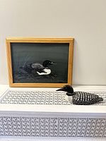 Photo showing both the framed loon painting and the wood loon carving placed side by side on a patterned surface.