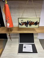 Front view of sun catcher featuring colorful birds on a wire and the orange pottery wind bell with hanging string and bird motif.