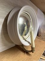Side angled view of the wall sconce showing the white heavy wood frame, convex mirror, and brass candle fixture.