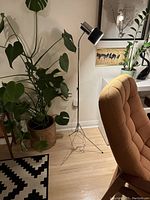 Full view of lamp in living space showing black shade, telescoping pole and tripod base