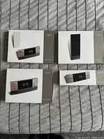 Top-down photo showing four boxed electronic weather instruments laid on fabric, including hygrometer and clock units with black screens and silver side panels.