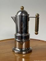 Front perspective view of the coffee maker showing stainless steel body with gold-tone handle and lid knob.