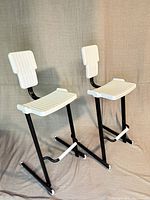 Front side view of two white plastic and black metal stools showing ribbed seats and backs