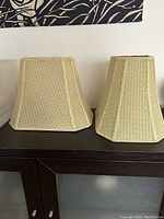 Frontal view of two corner cut rectangular fabric lamp shades, showing textured beige fabric and trapezoidal shape.