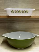 Side view of Fire King Meadow Green milk glass rectangular casserole dish with floral pattern and large Pyrex Verde Olive Green mixing bowl beneath it.