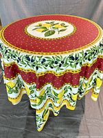 Square coated tablecloth draped over a round table showing the full design including central lemon motif and patterned borders.