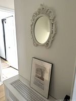 Wide view of white plaster oval mirror mounted on wall with framed London Underground print artwork below