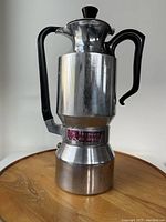 Front angle of the assembled aluminum stovetop coffee pot with black handle and knob showing overall condition and branding.