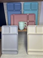 Five pastel-colored Tupperware divided dinner trays with two matching cups stacked on some trays