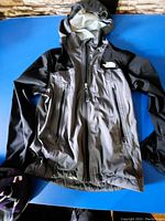 Front view of boys The North Face jacket laid flat on blue background showing hood, zippered pockets and logo on chest.