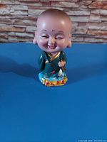 Photo of a 3-inch Buddha bobble head figurine with green robes and a decorated base.