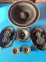 Top view showing one large 10 inch subwoofer speaker, two 6x9 speakers, one midrange speaker, and two tweeters arranged on a blue background.