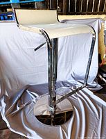 Single chrome bar stool with a white or light beige seat in good condition, showing curved frame and footrest.