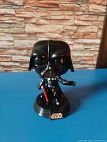 Photo of black and silver Darth Vader bobble head figure with detailed helmet and armor, holding a red lightsaber, mounted on black base with Star Wars logo.