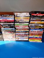 Three stacks of DVDs with visible titles from English and Indian cinema, arranged on a blue surface