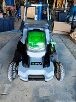 Front view of EGO electric lawn mower showing wheel treads, green translucent battery compartment cover with 56V marking, EGO logo on body.