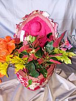 Front view of heart shaped floral box open showing orange and yellow artificial flowers with green leaves inside.