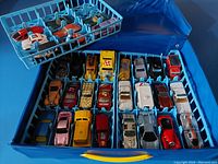 Top view of two light blue organizer trays holding 48 Hot Wheels toy cars of various models and colors inside the blue plastic carrying case.