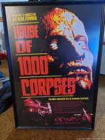 Framed House of 1000 Corpses movie poster showing skull face with eyes and large red text. Poster is in good condition with vibrant colors.