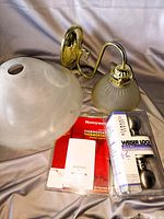 Photo showing a wall-mounted light fixture with brass/gold-tone mount and frosted glass dome shade, a Weser Lock door knob in packaging, and a Honeywell thermostat with packaging.