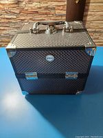Closed black textured makeup box with silver metal accents, handle, and latches.