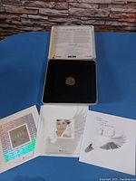 Top view of the open black velvet presentation case holding the 1999 coin with three Canadian millennium stamps and certificates below.