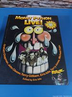 Front cover of Monty Python Live! coffee table book showing caricature of Monty Python members and title text.