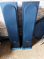 Front view of two Panasonic tower speakers standing upright with black protective grille covers and black finish.