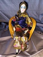 Porcelain doll in velvet and brocade outfit seated in small wooden chair, showing front and detail of doll and chair.