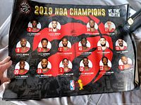 Photo showing a 2019 Toronto Raptors NBA Championship poster featuring player headshots, names, and jersey numbers.