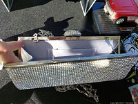 Open view of the shiny jewelled purse showing the interior light gray lining and chain strap attached to metal frame with jeweled clasp closure.