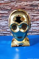 Closed gold and blue C-3PO head with reflective metallic finish showing front view on blue surface.