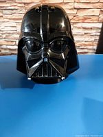Front view of the Darth Vader black plastic helmet with visible face details and silver mouthpiece elements.