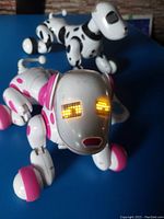 Two robotic dog toys, one white with pink spots, another white with black spots, shown with glowing LED eyes.
