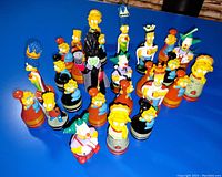 Full set of The Simpsons themed chess pieces arranged on blue background showing all characters and variety of painted details.