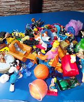 Wide angle photo showing the collection of an assortment of cartoon character toys, small vehicles, and colorful plastic items scattered on a blue surface.