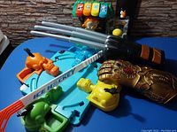 Photo showing the Marvel Infinity Gauntlet toy, mini table hockey game with player pieces, and toy gun arranged on a table against a brick wall.
