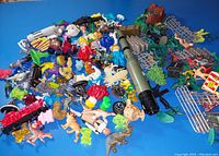 Overview of assorted mixed toy lot spread on blue table showing multiple small toys including army men and other figures