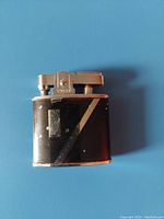 Front side photo showing black and silver vintage Omega lighter, with signs of wear and some scratches
