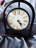 Front view of the vintage style mantle clock showing the round face with Roman numerals and the arch-shaped dark frame.