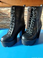 Side and angled view showing black platform combat boots with thick high heels and lace-up fronts.