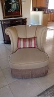 Front view of armless accent chair showing upholstery, lumbar pillow, and fringe trim.