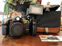 Canon MGM-1 motor drive film camera with attached flash and camera bag. Camera lens cap in place, user manual or brochure included.