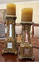 Two ornate gilded candleholders with etched glass, different heights on a wooden table.