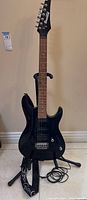 Full front view of the Ibanez Gio GSA60 black electric guitar on the stand including visible strap and coiled power cord on floor.