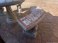 Concrete curved patio bench with mosaic tile top showing side and front details on stamped concrete surface.