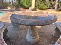 View of the full concrete patio table with tile top and curved benches around it, outdoors by a pool.