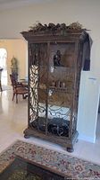 Front view showing full cabinet with scrolled iron doors, wood crown and base, decorative top swag