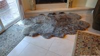 Overall view of large grey sheepskin rug laid on tiled floor near sliding glass door.