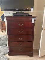 Front view of the wood tallboy dresser with five drawers and metal handles in dark wood finish.